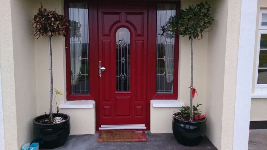 Red entrance door with potted plants on sides.