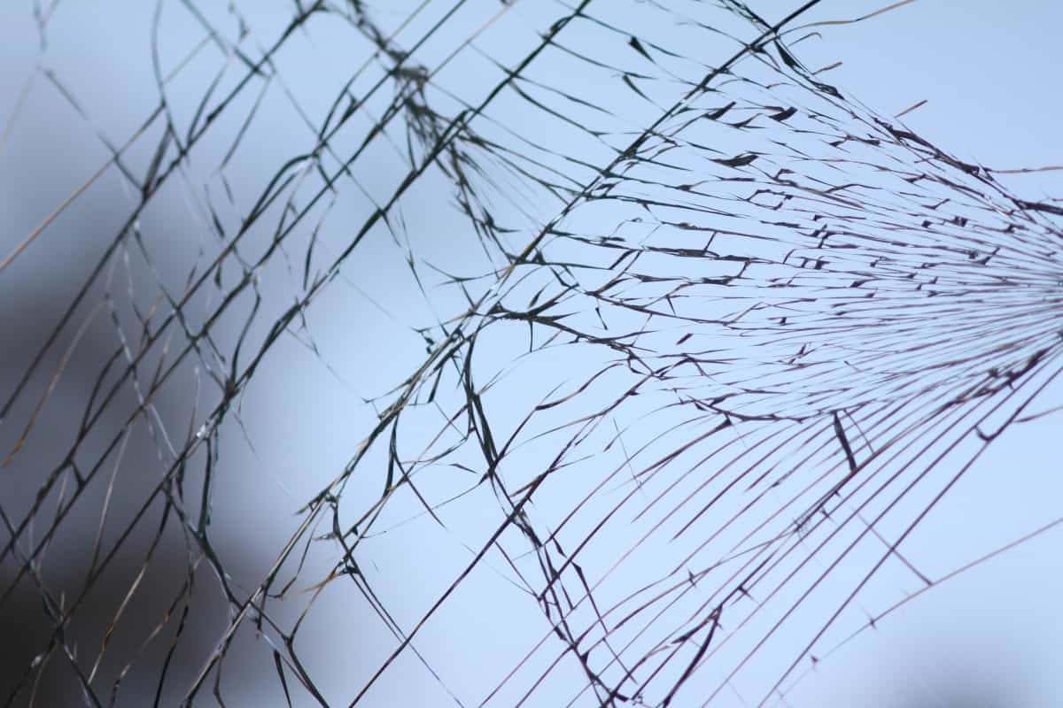 Close-up of cracked glass against blue sky.